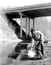 a man with a trash bag pulling a hub cap from the creek